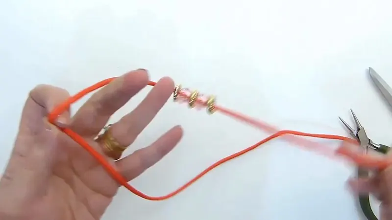 Una mano sostiene un lazo de soga naranja mientras la otra sujeta el extremo, con los abalorios a un lado