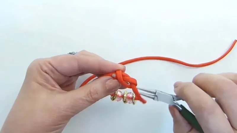 Una pinza de punta redonda sujeta el extremo de la soga naranja al formar el primer nudo corredizo