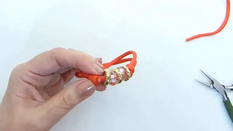 Una mano sostiene la pulsera de soga naranja con los dos nudos corredizos y los abalorios en el centro