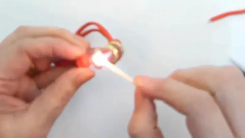 Dos manos acercan una llama a la punta de la soga naranja de la pulsera para sellarla
