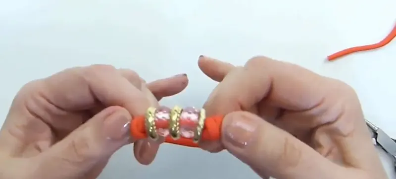 Dos manos tiran de la pulsera de soga naranja para mostrar cómo se desplazan los nudos corredizos