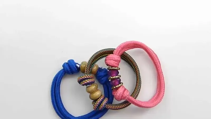 Tres pulseras de soga con nudo corredizo, una azul, una rosa y una de rayas de colores, con abalorios y arandelas doradas